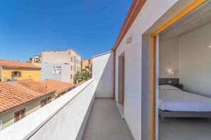 Un balcón con cama, ventana y vista a edificios vecinos.