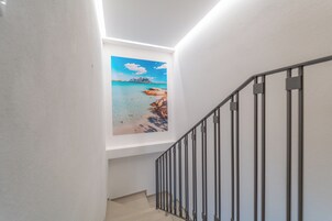 Un escalier avec une rampe, un tableau représentant une scène de plage et un mur blanc.