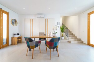 Un espace repas moderne avec une table en bois, deux chaises colorées, un ordinateur portable et une plante en pot.