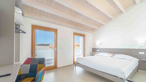 Un dormitorio con una cama, una silla colorida y una puerta al balcón.
