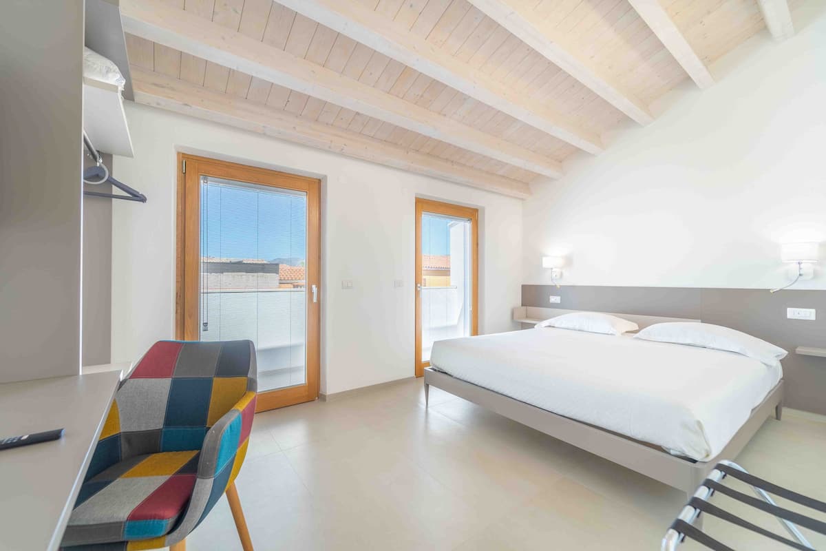 Un dormitorio con una cama, una silla colorida y una puerta al balcón.