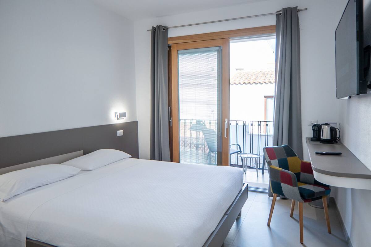 Una habitación de hotel con cama, una silla, una mesita y un balcón con vistas.