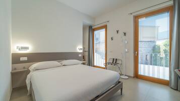 Una moderna camera d'albergo con un letto grande, un tavolino, una lampada da comodino, una sedia, una finestra con vista e una porta scorrevole verso il balcone.