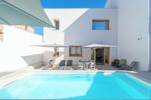 Un espace piscine extérieur moderne, doté de chaises longues et de parasols, avec un ciel bleu dégagé et un bâtiment blanc aux fenêtres.