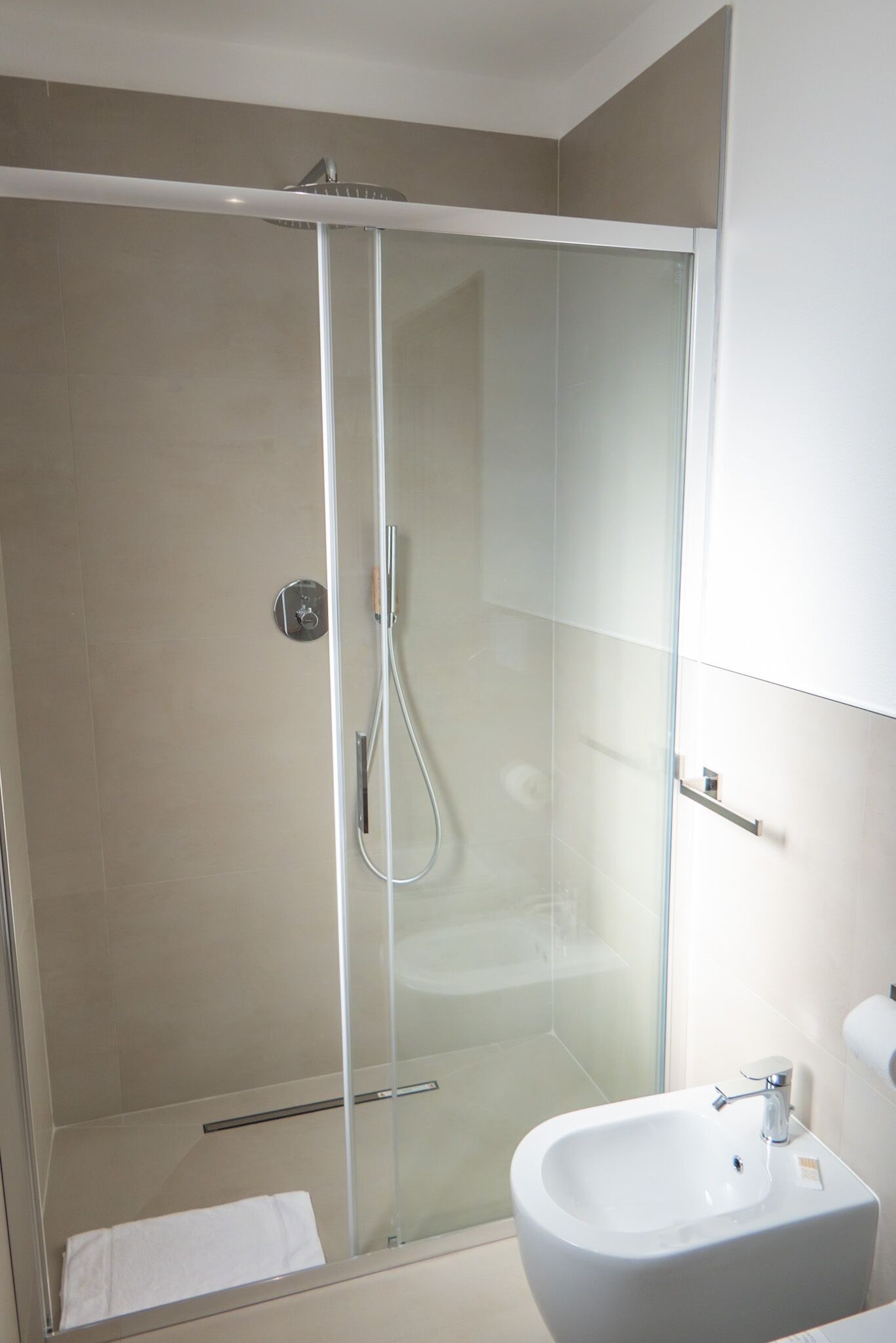 Un bagno moderno con doccia vetrata, lavabo bianco e porta asciugamani.