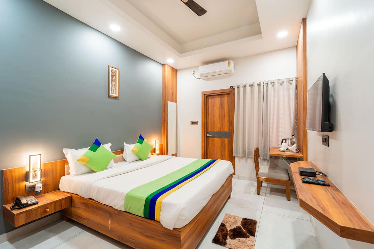 A modern hotel room with a wooden bed, bedside tables, a desk, and a television.