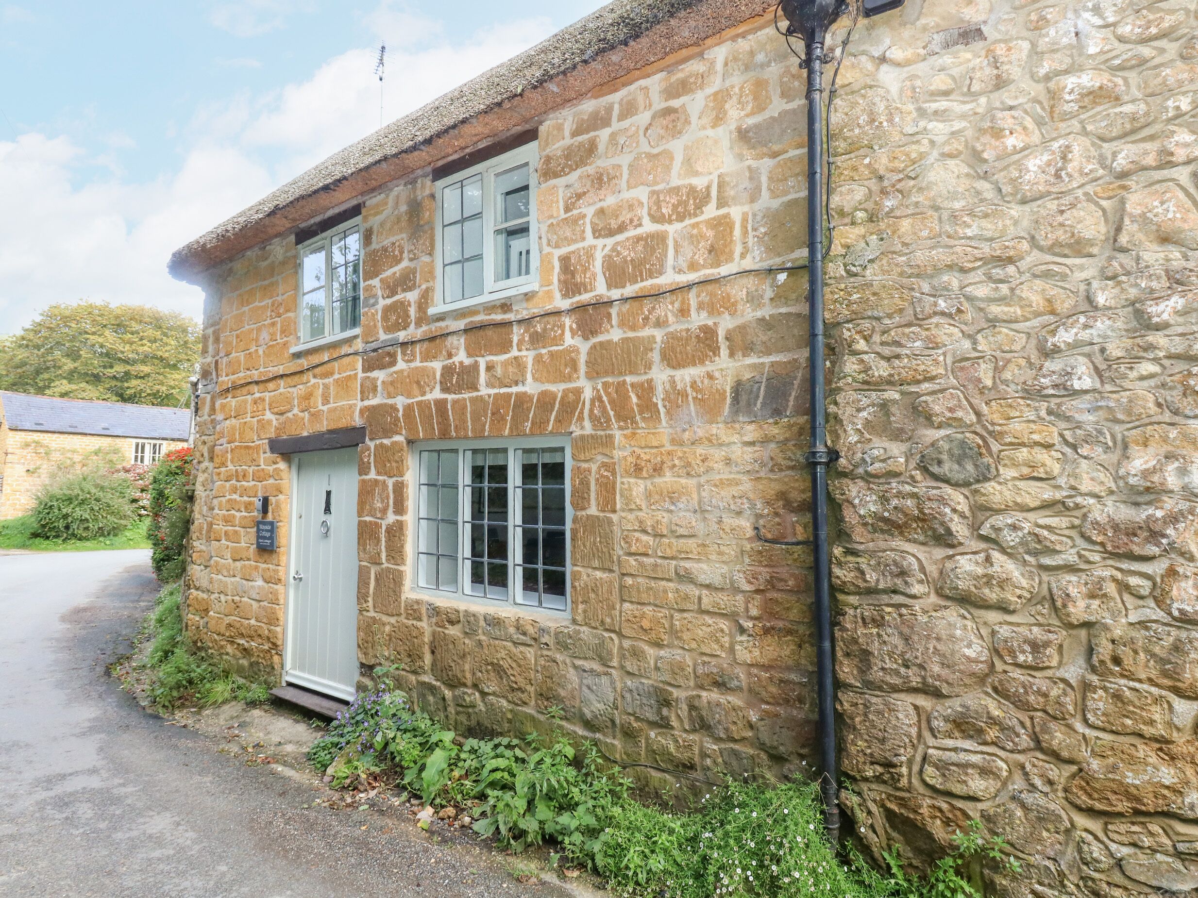 A stone building with a white door and windows, a narrow driveway, and a stone wall.