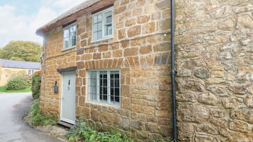 A stone building with a white door and windows, a narrow driveway, and a stone wall.