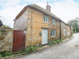 A stone building with a thatched roof, a wooden door, and a small garden area with plants.