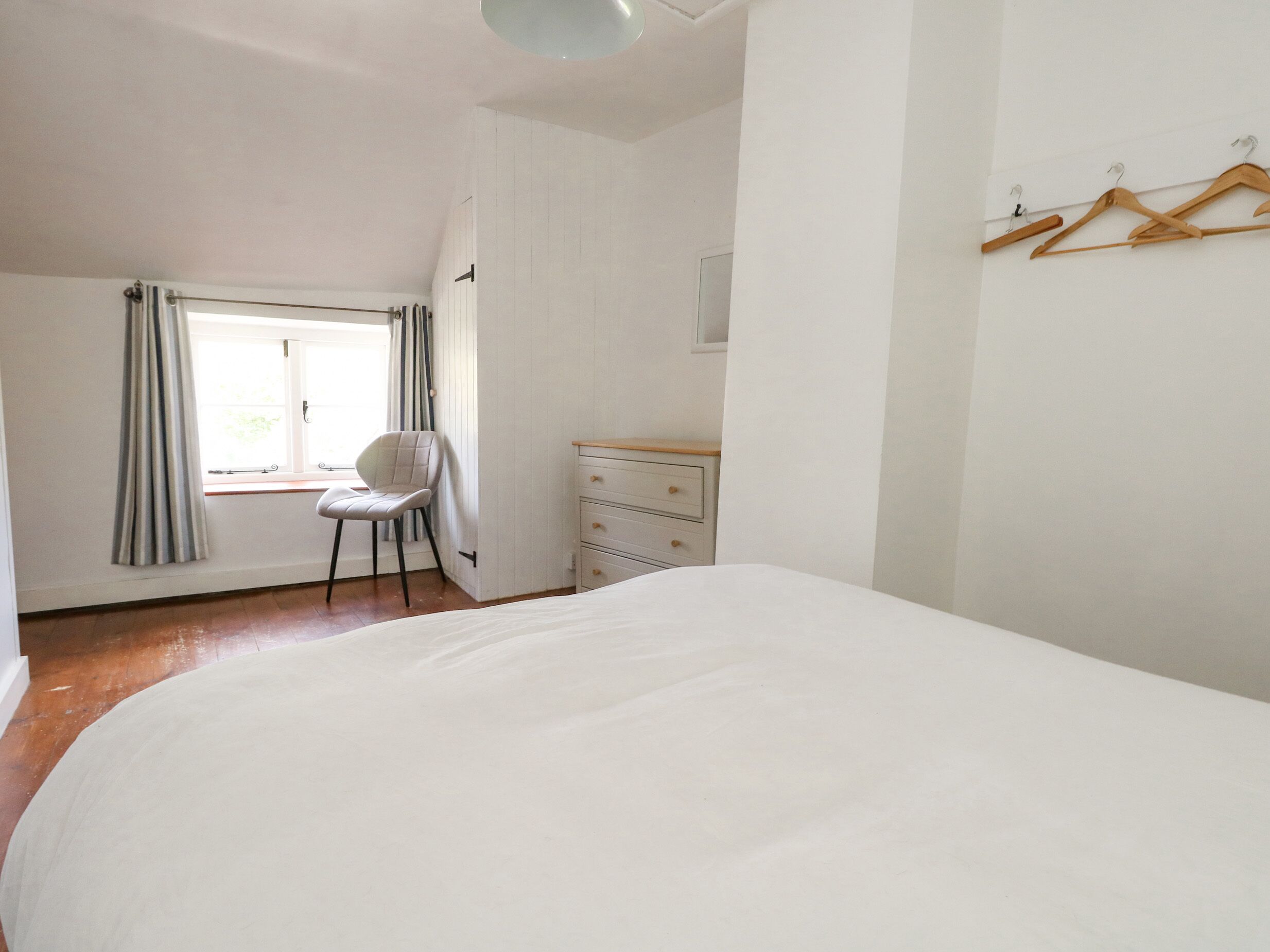 A bedroom with a large bed, a chair, a dresser, and a window with curtains.