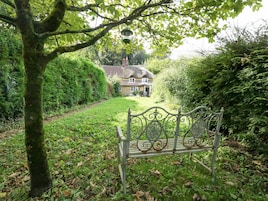 A bench in a lush garden with a thatched-roof house in the background.