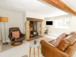 Una sala de estar con chimenea de piedra, mobiliario de cuero, televisor y ventana con persianas.