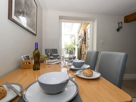 A dining area with a table set for two, featuring a bowl, plates, a wine bottle, and a biscuit.