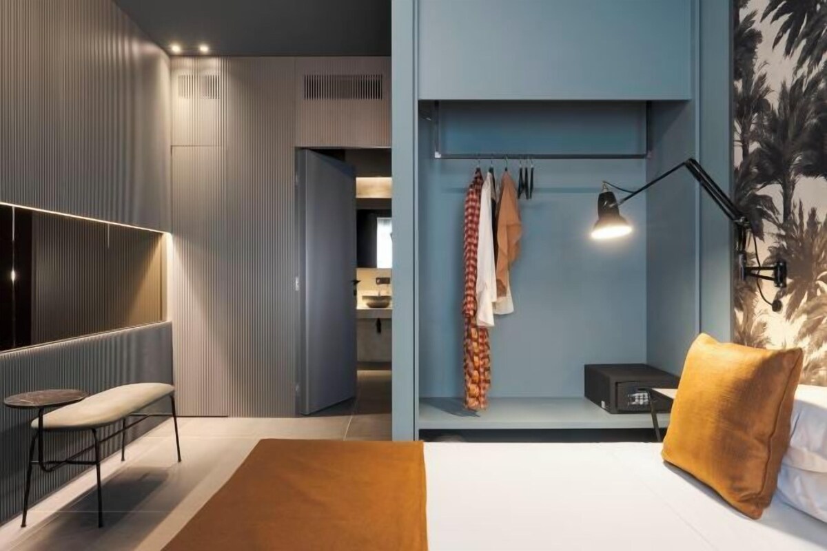 A modern bedroom with a bed, a bedside table, a bench, a hanging light, and a wardrobe.