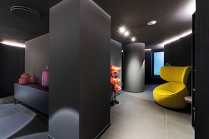 Un interno moderno con un design minimalista, caratterizzato da una consolle nera, una sedia gialla e un'imponente colonna cilindrica.