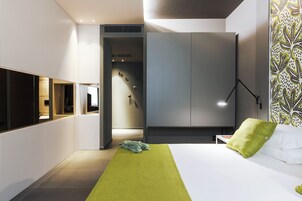 Una camera d'albergo moderna con un letto grande, un tappeto verde, un armadio e una TV a parete.