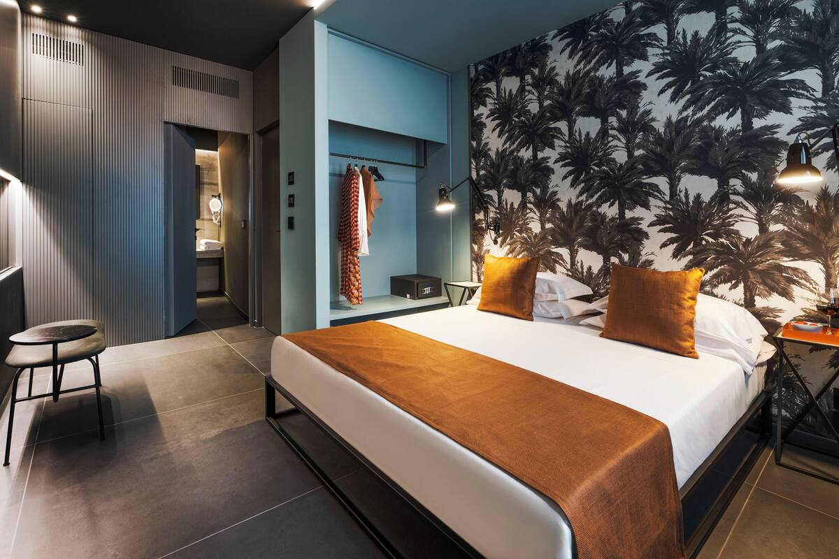 A modern hotel room with a large bed, a nightstand, a desk, and a chair.