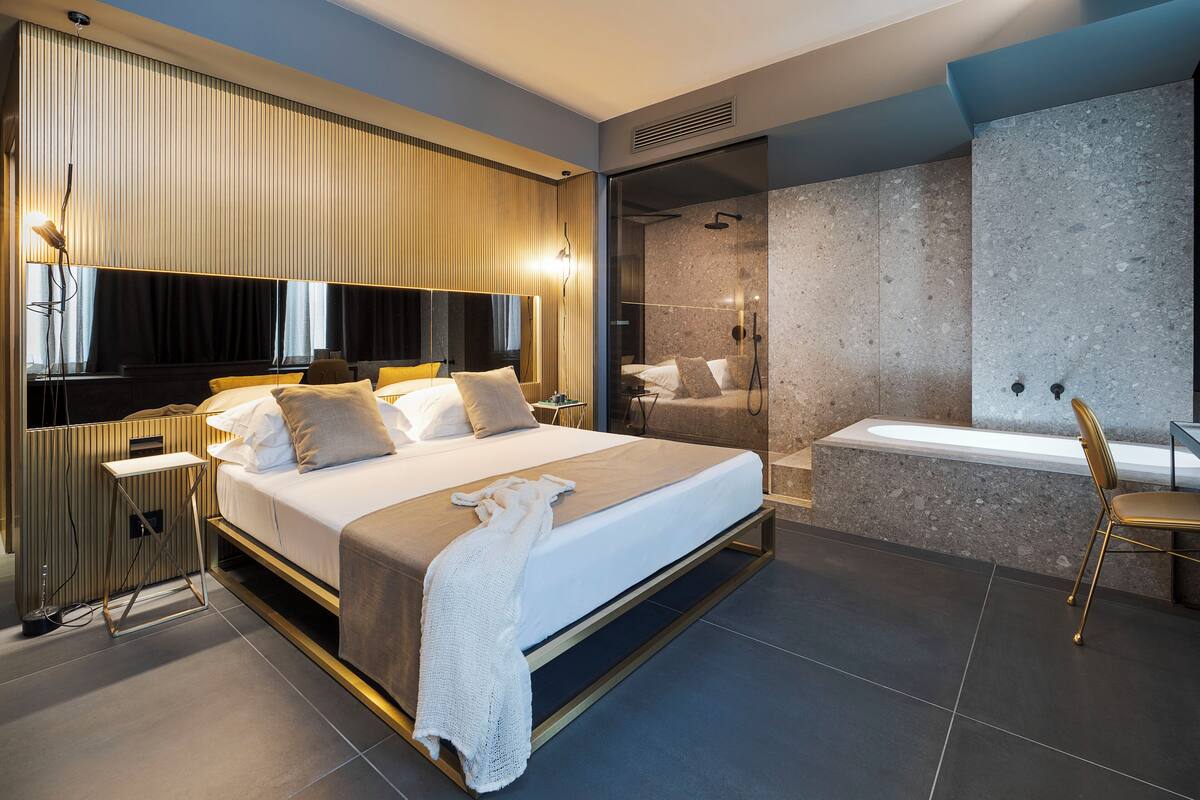 A modern bedroom with a large bed, bedside tables, a built-in wardrobe, and a bathroom with a bathtub and shower.