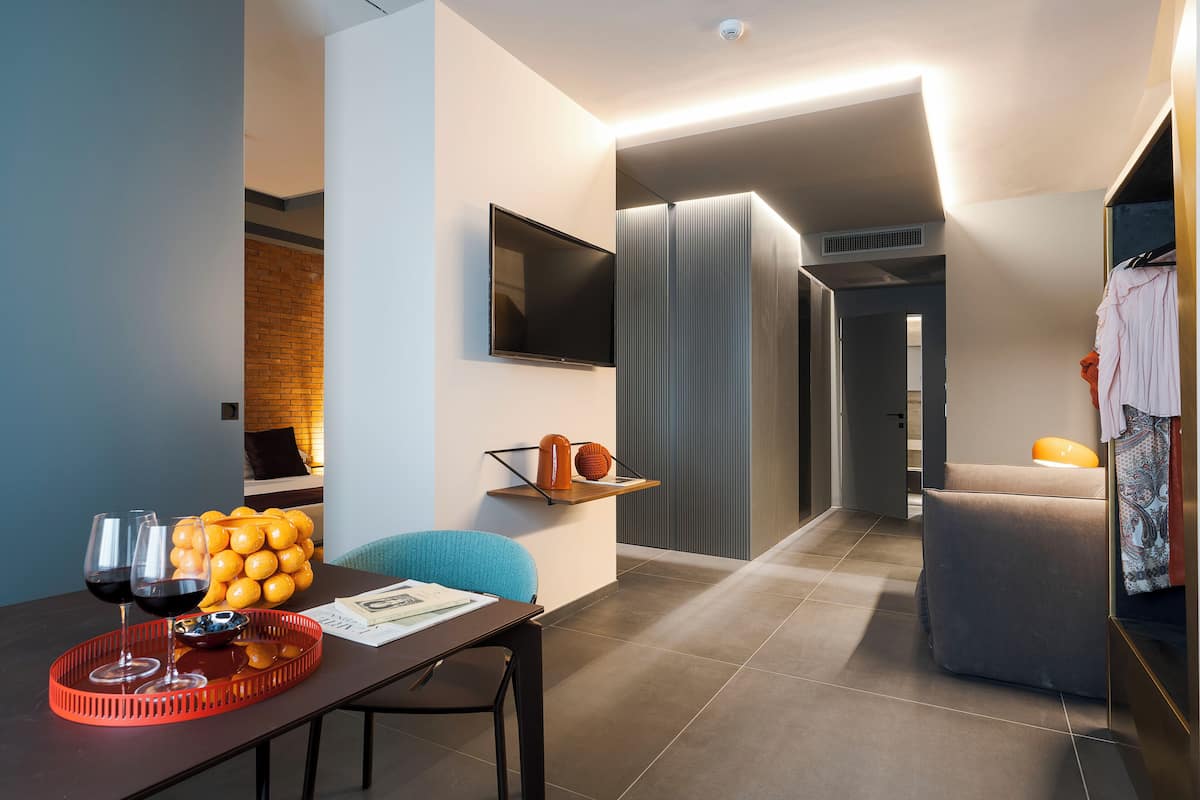 A modern hotel room with a dining area, a flat-screen TV, a seating area, and a wardrobe.