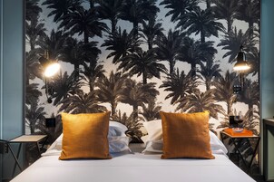 Camera d'albergo con un letto, due cuscini, un comodino, una lampada e una parete con un murale di palme.