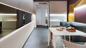 Et moderne hotelværelse med spiseplads, en sofa og et bord med glas og bakke.