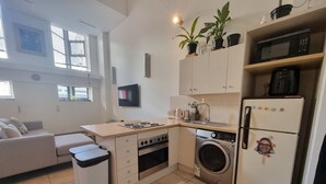 A compact kitchen with a washing machine, microwave, and a small dining area with a sofa. - Mutual Heights M15 by CTHA (Cape Town)