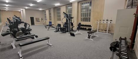 Un gimnasio con diverso equipo de ejercicio, como cintas de correr, bancos de pesas y mancuernas.