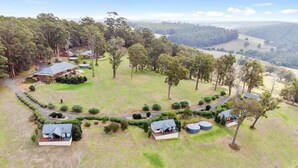 An aerial view of a rural property with several houses, surrounded by dense forests and rolling hills. - Scarlet Woods Chalets (Quinninup)