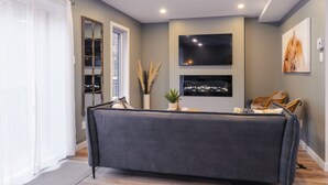 Una sala de estar moderna con un sofá gris, un televisor montado y un cuadro en la pared.