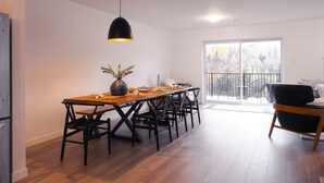 Un comedor con una mesa y sillas de madera, una lámpara colgante y vistas a un balcón con mobiliario exterior.
