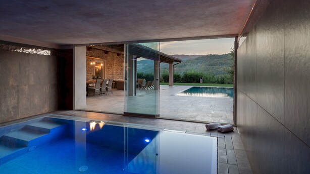 Ein moderner Poolbereich im Innenbereich mit freiem Blick auf eine Außenanlage und einen Pool.