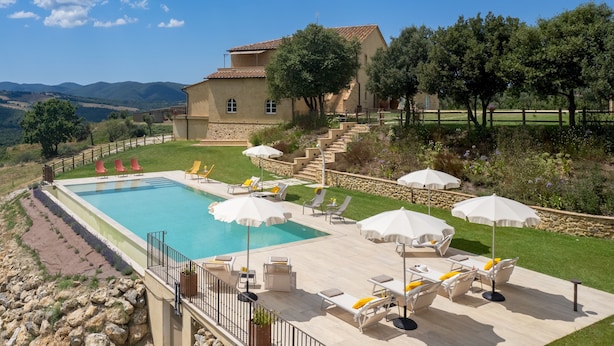 A pool area with lounge chairs and umbrellas, surrounded by a stone wall and a view of a hill and trees. - Casolare San Martino 12, Emma Villas (Pomarance)