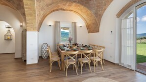 A dining area with a brick arch, wooden flooring, and a table set for six with chairs. - Casolare San Martino 12, Emma Villas (Pomarance)