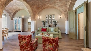 A spacious living room with a high arched ceiling, a green sofa with red cushions, floral armchairs, and a wooden coffee table. - Casolare San Martino 12, Emma Villas (Pomarance)