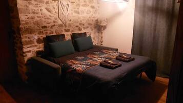Quarto aconchegante com parede de pedra, cama com colcha florida, duas almofadas e mesa de cabeceira com luminária.