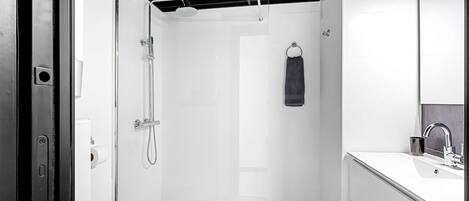 A modern bathroom with a glass-enclosed shower, a white sink with a mirror, and a black tiled floor.