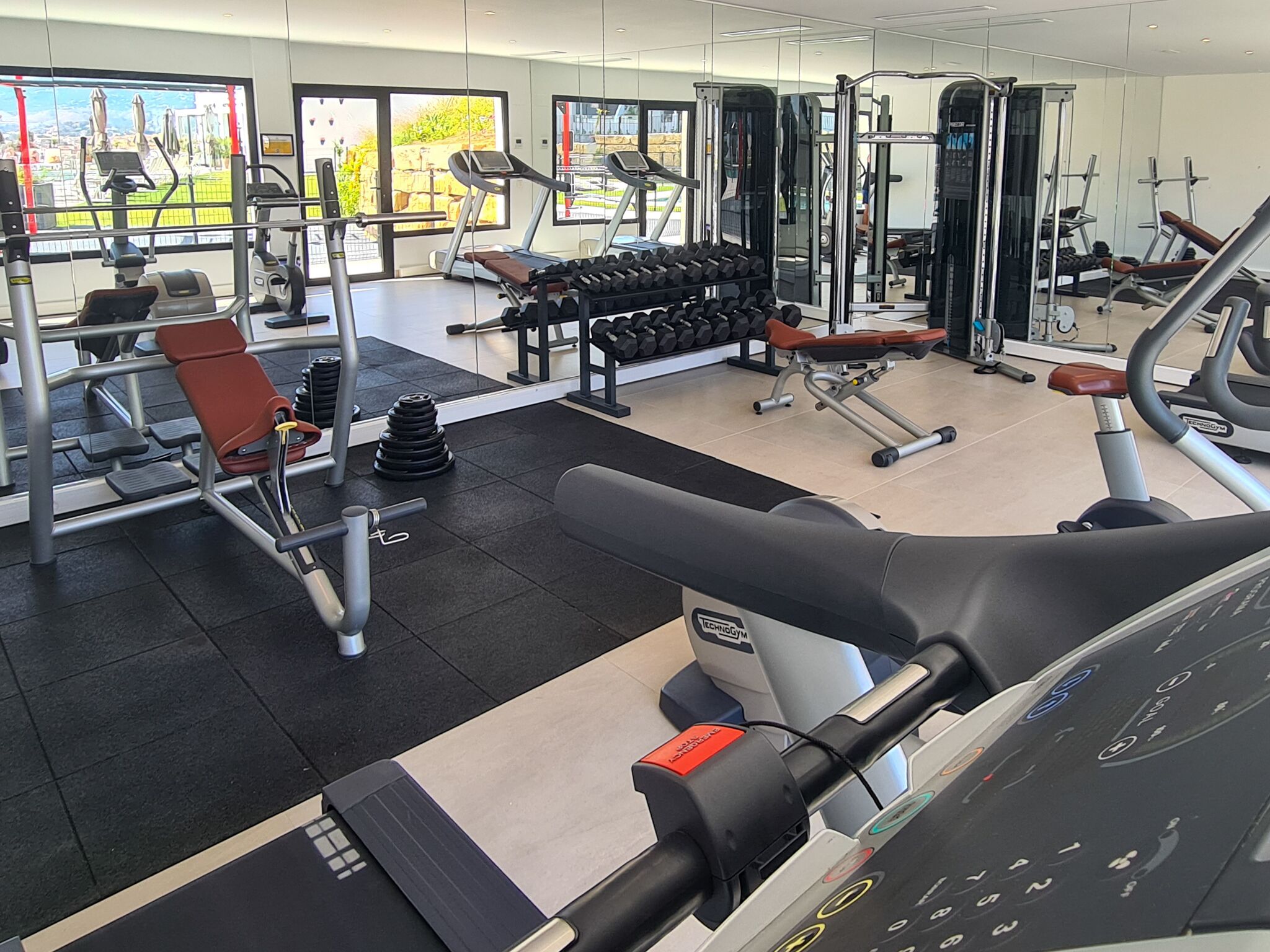 A gym with cardio machines, weightlifting equipment, and dumbbells.