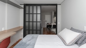 A modern bedroom with a bed, a desk, and a dining area. - Apto 2 quartos no Centro de BH (Belo Horizonte)
