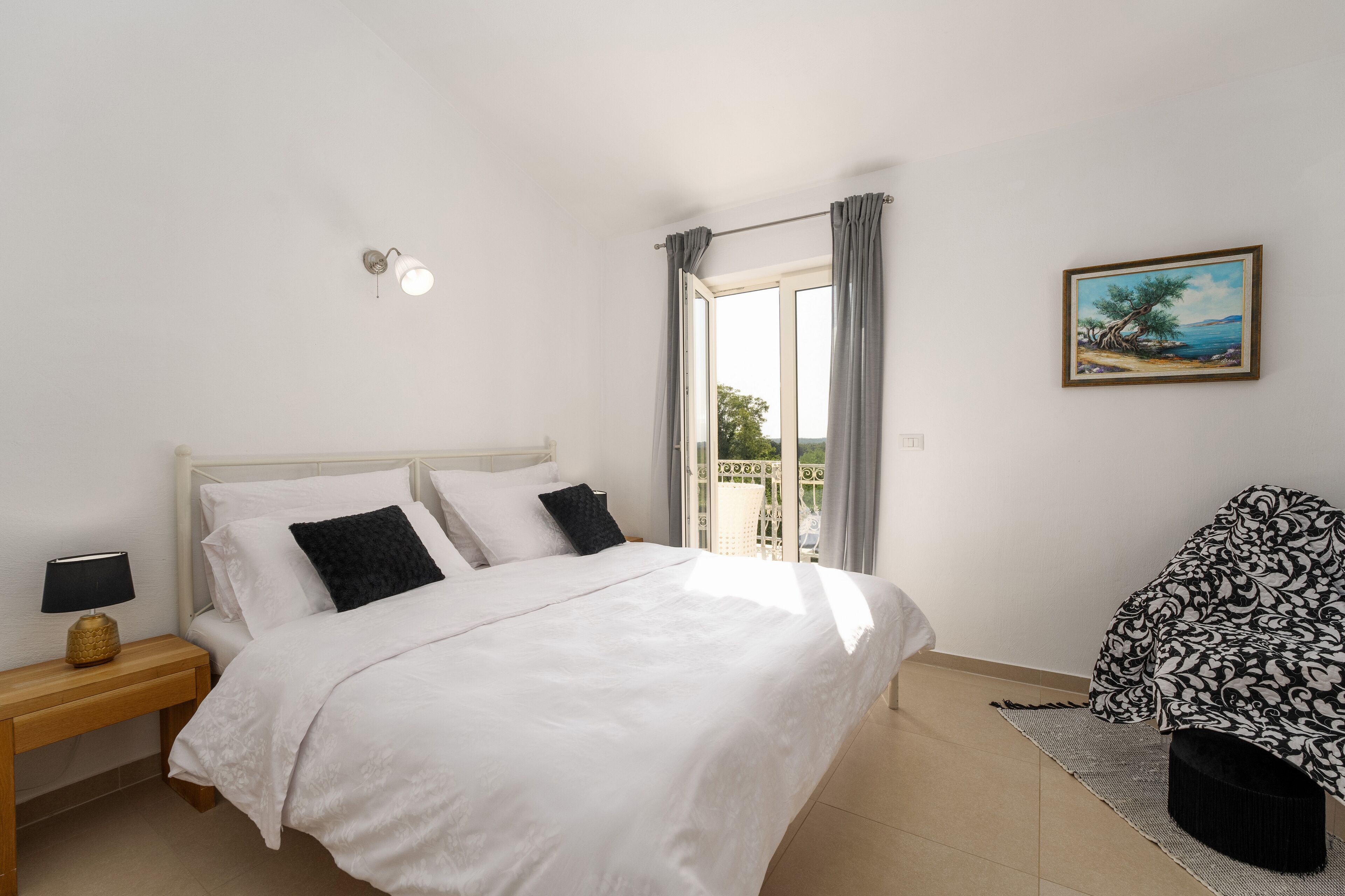 A bedroom with a bed, a nightstand, a chair, a painting, and a window with curtains.