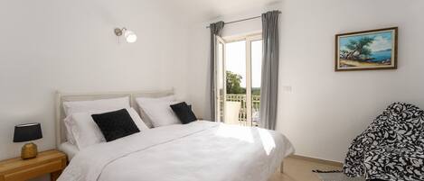 A bedroom with a bed, a nightstand, a chair, a painting, and a window with curtains.