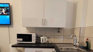 Een kleine keuken met witte kastjes, een magnetron, een waterkoker en een spoelbak.