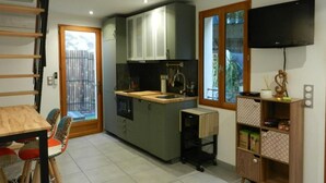 A compact kitchen with a built-in oven, a small island, and a TV mounted on the wall. - The little house (Ceyreste)