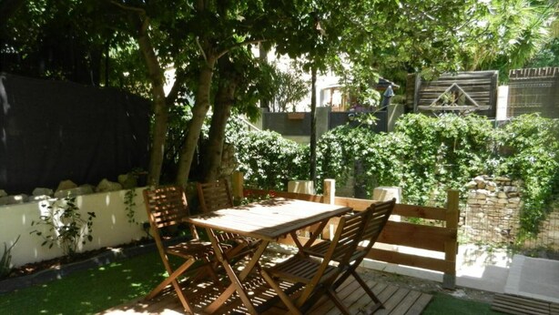 A wooden table and chairs set outdoors with a grassy area and trees in the background. - The little house (Ceyreste)