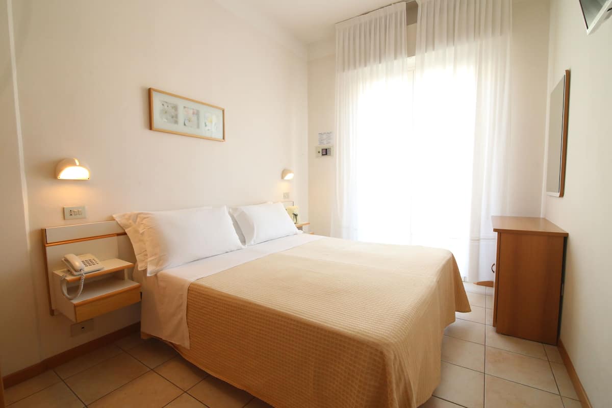 A neatly made bed with a beige bedspread, a bedside table with a lamp, a phone, and a framed picture on the wall.