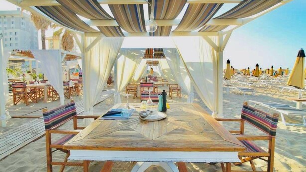 An outdoor dining area with a wooden table and chairs, surrounded by white canopies and beach umbrellas. - Hotel Soave Miriam (Rimini)