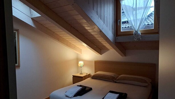 Un dormitorio con cama, mesita de noche, lámpara y ventana con cortinas translúcidas.