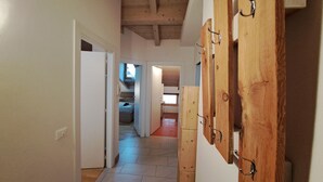 Un pasillo estrecho con vigas de madera en el techo, una puerta de madera a la derecha y una cama al fondo.