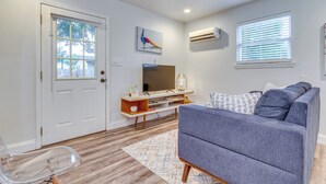 A living room with a grey sofa, wooden entertainment unit, and a TV. - 'the Dragonfly House' - Walk to Downtown Pensacola (Pensacola)