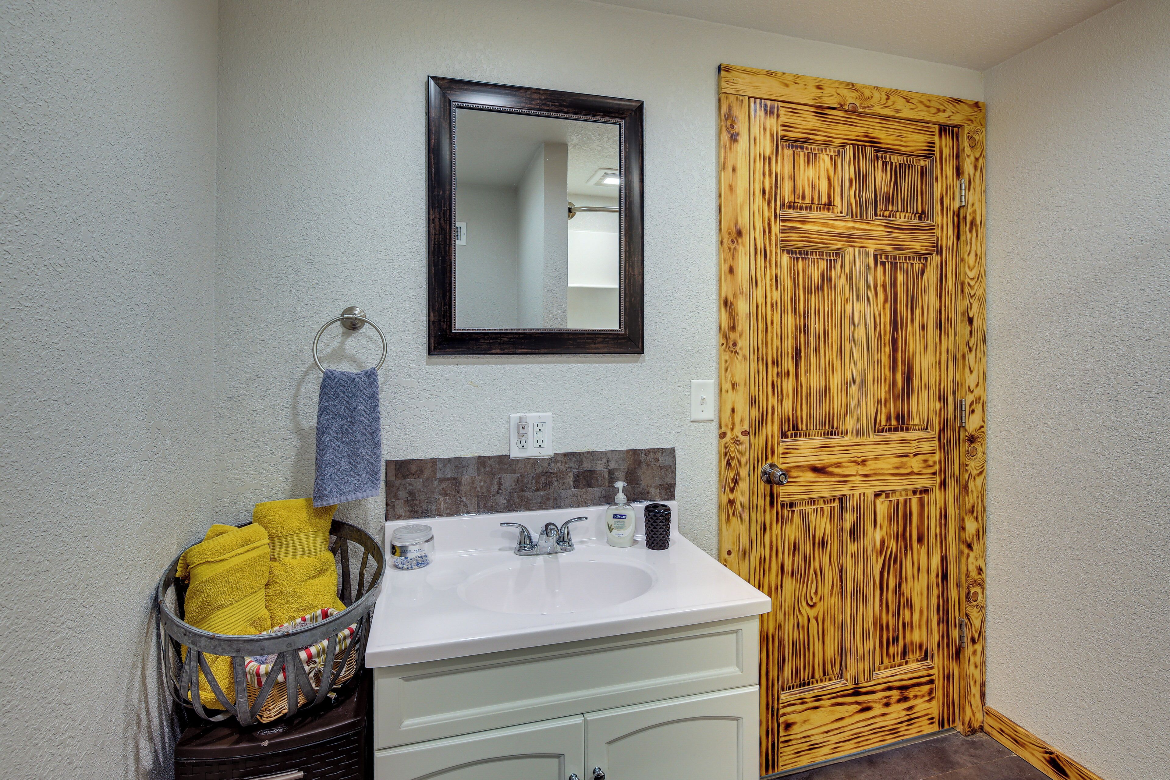 A bathroom with a white sink, a mirror, a wooden door, and a basket of towels.