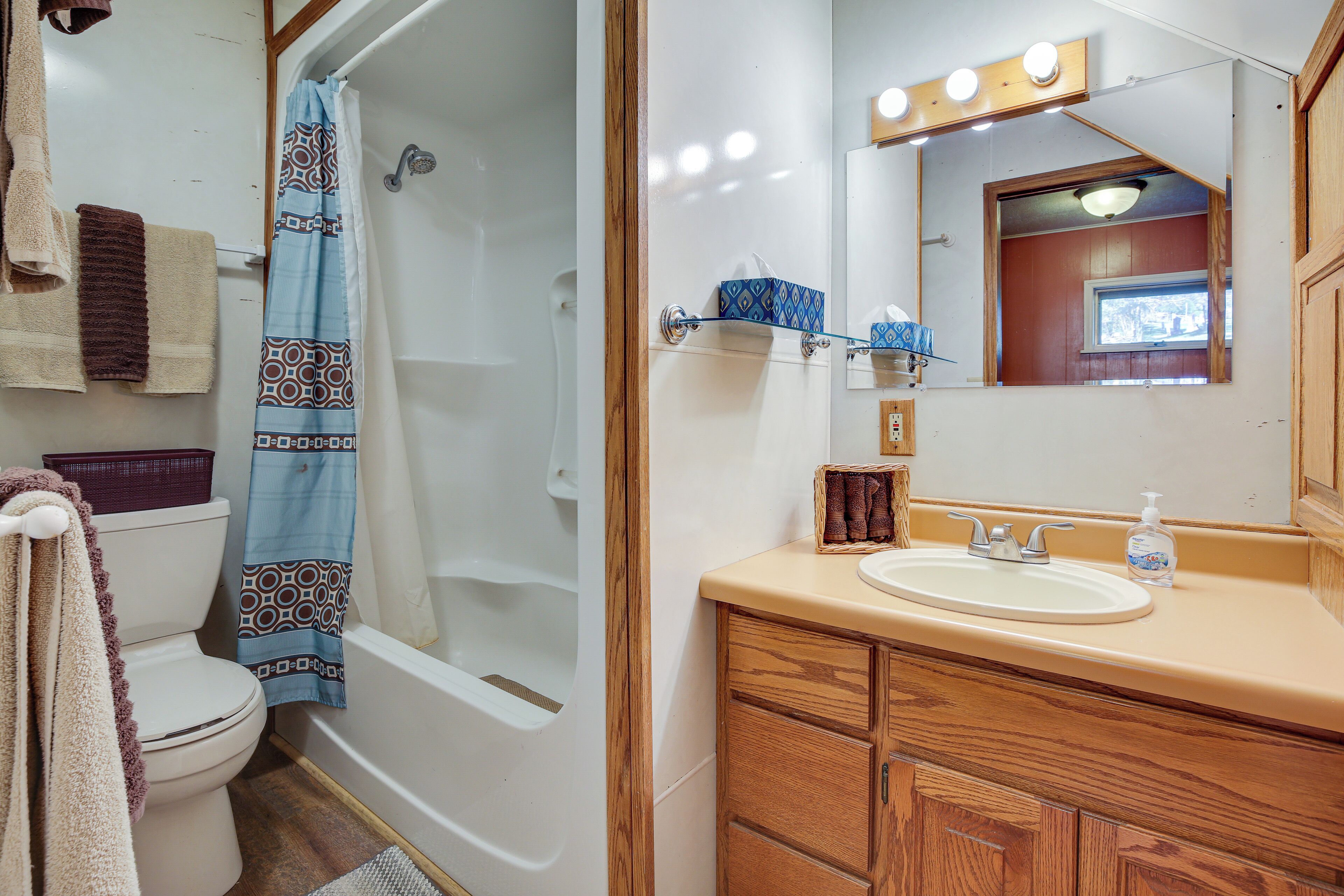 A bathroom with a toilet, shower, sink, and wooden cabinets.
